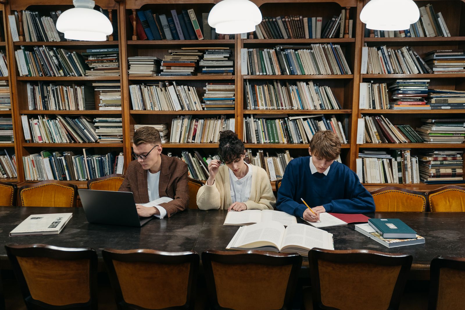 International university students studying with books, notebooks, and a laptop in a library
