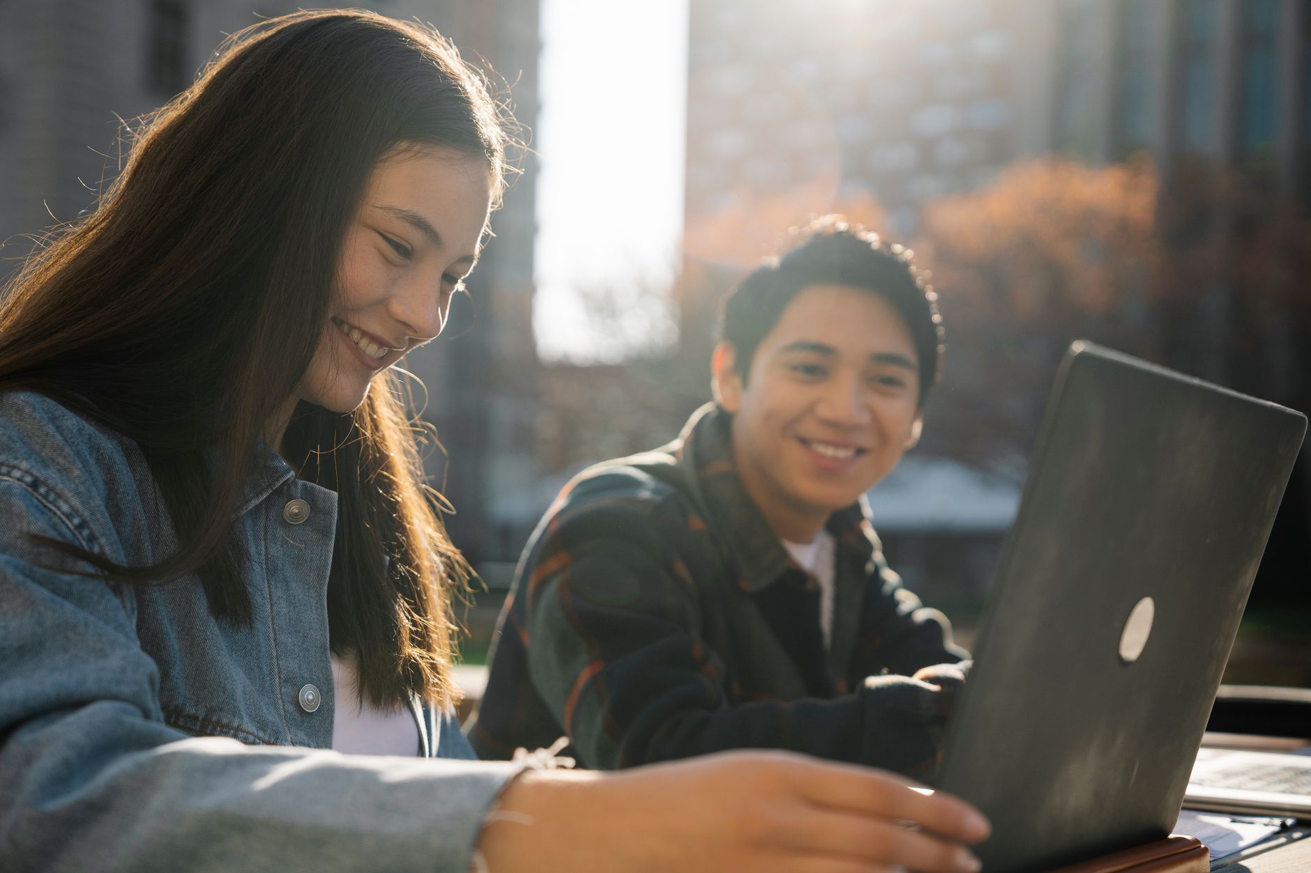 boy and a girl studying together outdoors in front of a laptop